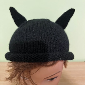Peut inclure: Chapeau noir en tricot avec deux petites cornes sur le dessus. Le chapeau est sur une tête de mannequin.