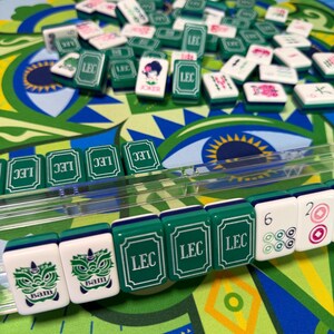 Puede incluir: Primer plano de un juego de Mahjong con fichas verdes y blancas. Las fichas presentan varios s&iacute;mbolos y caracteres, incluido el texto "LEC" y "Bam". El juego est&aacute; sobre un tapete con dise&ntilde;os verdes y azules.