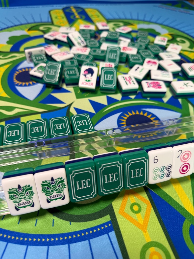 Puede incluir: Primer plano de un juego de Mahjong con fichas verdes y blancas. Las fichas presentan varios s&iacute;mbolos y caracteres, incluido el texto "LEC" y "Bam". El juego est&aacute; sobre un tapete con dise&ntilde;os verdes y azules.