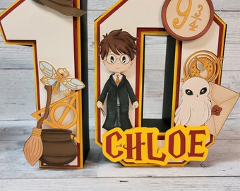 May include: A 3D number 10 cake topper with a Harry Potter theme. The number 10 is decorated with a brown wizard hat, a broomstick, a cauldron, a golden snitch, a white owl, and a character from the Harry Potter series. The number 10 is also decorated with the name "CHLOE" in yellow letters.