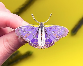 Puede incluir: Pin de esmalte de mariposa púrpura y blanca con detalles dorados. La mariposa tiene alas detalladas con un patrón de púrpura, blanco y dorado.