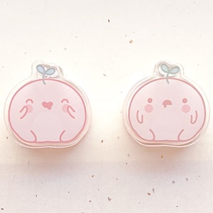 May include: Two pink cartoon character charms with a green leaf on top. One charm has a heart and a smile, the other has a frown and two dots for eyes.