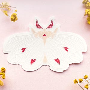 May include: White moth sticker with red hearts on its wings. The moth has a delicate, feminine design and is perfect for adding a touch of whimsy to any project.