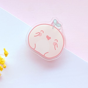 May include: A pink and white cartoon character with a small green leaf on its head. The character has a heart-shaped nose and is smiling. The character is made of clear acrylic.