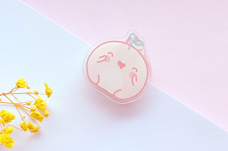 May include: A pink and white cartoon character with a small green leaf on its head. The character has a heart-shaped nose and is smiling. The character is made of clear acrylic.
