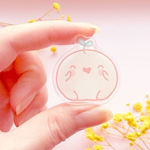 May include: A clear acrylic charm with a pink and white cartoon character with a heart and a small green leaf on top.