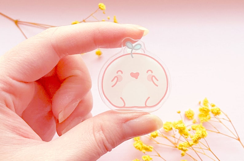 May include: A clear acrylic charm with a pink and white cartoon character with a heart and a small green leaf on top.