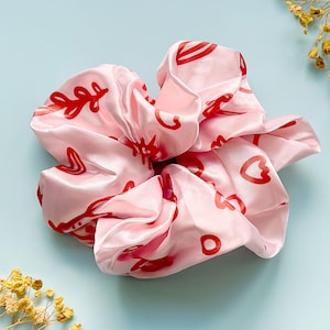May include: Pink satin hair scrunchie with a red and white abstract design featuring hearts and leaves.