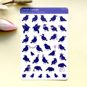 Puede incluir: Una hoja de pegatinas con ilustraciones de cuervos azul oscuro con detalles blancos. Los cuervos se representan en varias poses, algunos con sombreros o sosteniendo objetos. La hoja tiene el texto "Corvid Curiosity" en la parte superior.