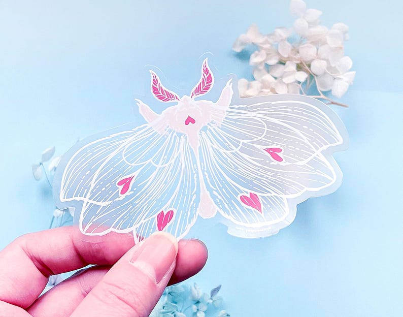 May include: A clear sticker with a white moth design. The moth has pink hearts on its wings.