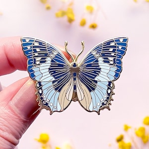 May include: A gold-tone butterfly pin with blue and white wings. The butterfly has a detailed design with a textured finish.