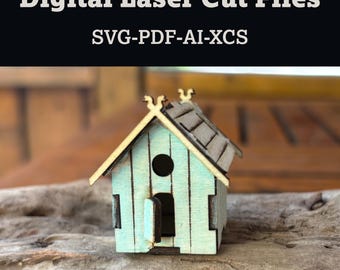 Può includere: Una casetta in legno in miniatura con esterno azzurro chiaro e tetto grigio. La casa ha un'apertura rotonda e una porta aperta. Il testo "Digital Laser Cut Files" e "SVG-PDF-AI-XCS" è visualizzato nella parte superiore dell'immagine.