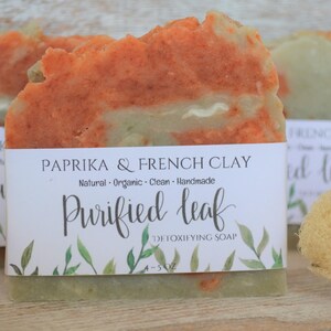 May include: A bar of handmade soap with a label that reads "Paprika & French Clay Purified Leaf Detoxifying Soap". The soap is a mix of orange and green colors.