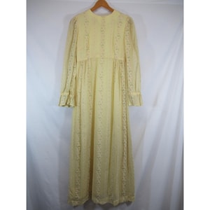 May include: A pale yellow, long-sleeved dress with a floral pattern and ruffled cuffs. The dress is hanging on a wooden hanger against a white background. The dress has a high neckline and a flowing, floor-length skirt.