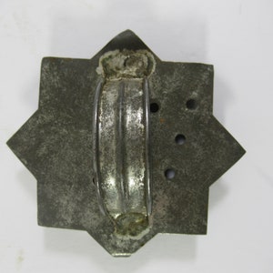 May include: A vintage metal cookie cutter shaped like a star with a handle. The cutter is made of tin and has a worn, aged look. It has several holes punched in the metal.