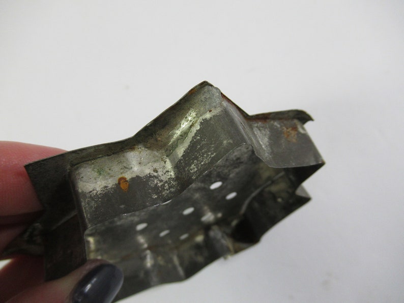 May include: A vintage metal cookie cutter shaped like a star with a worn, silver finish and rust spots. The cutter has small holes along the edges.