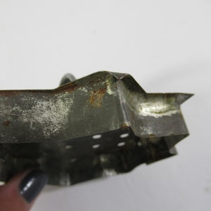 May include: A vintage metal cookie cutter shaped like a star. The cutter is made of tin and has a worn, rustic look. It has a few small holes in the bottom.