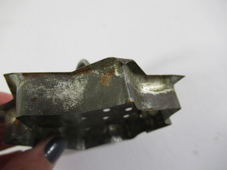 May include: A vintage metal cookie cutter shaped like a star. The cutter is made of tin and has a worn, rustic look. It has a few small holes in the bottom.