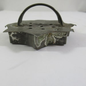 May include: A vintage metal cookie cutter shaped like a star with a handle. The cutter has a worn, rustic look with some rust spots and a faded design.