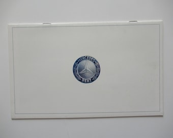May include: A white booklet with a blue and silver Mercedes-Benz logo on the front.