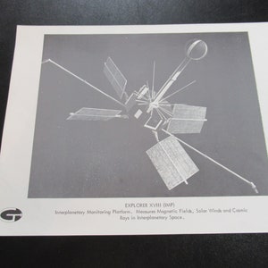 May include: A black and white photograph of the Explorer XVIII (IMP) satellite. The satellite is a multi-faceted, interplanetary monitoring platform that measures magnetic fields, solar winds, and cosmic rays in interplanetary space. The image is labeled with the text "EXPLORER XVIII (IMP)" and "Interplanetary Monitoring Platform. Measures Magnetic Fields, Solar Winds and Cosmic Rays in Interplanetary Space."