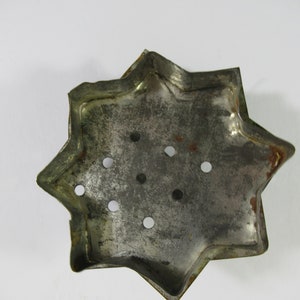 May include: A silver metal star-shaped cookie cutter with eight points and multiple holes. The cutter is slightly worn and has a rustic look.
