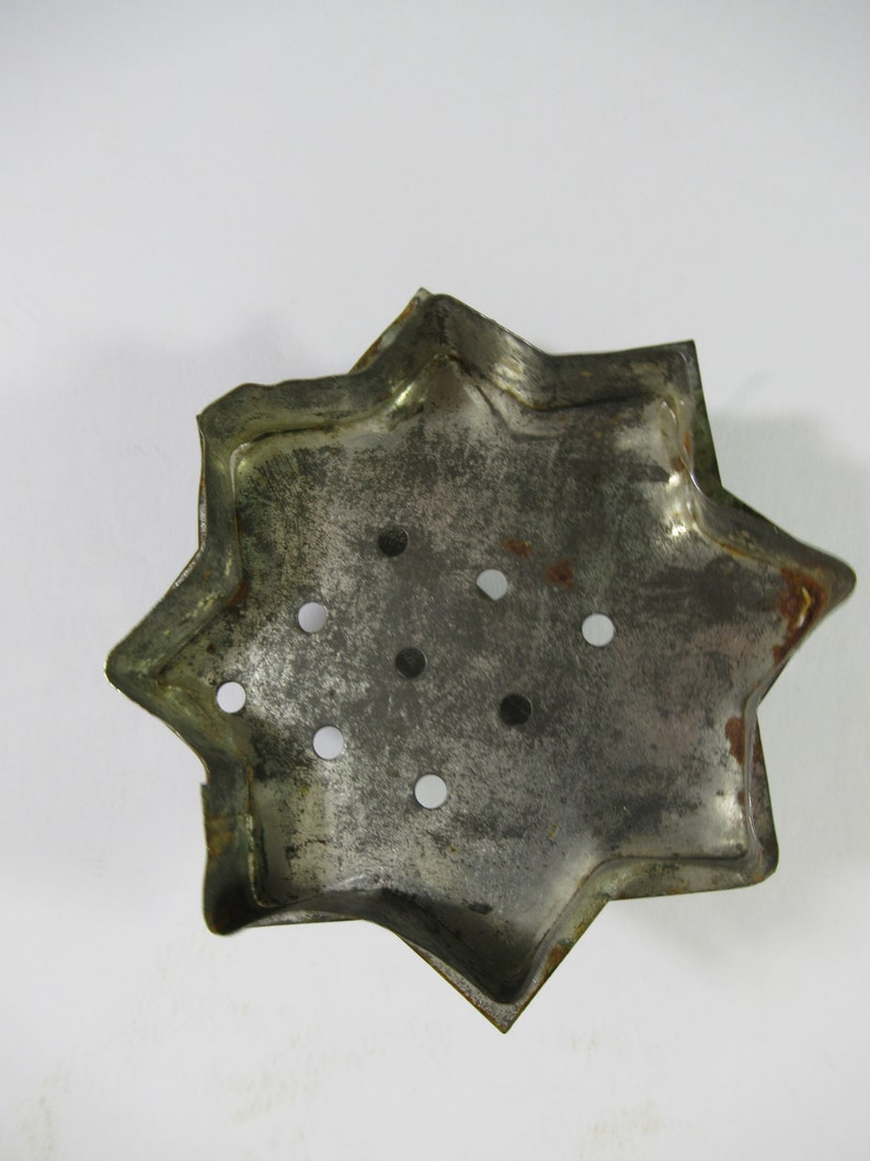 May include: A silver metal star-shaped cookie cutter with eight points and multiple holes. The cutter is slightly worn and has a rustic look.