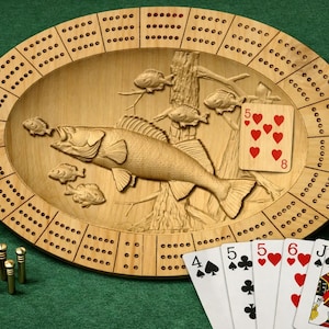 May include: Wooden cribbage board with a carved fish design, playing cards, and pegs. The board is oval-shaped with a fish carving in the center and holes for scoring. A deck of cards and pegs are next to the board.