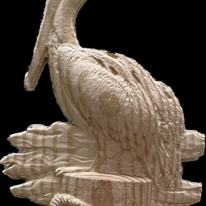 May include: A carved wooden pelican sculpture. The pelican is perched on a wooden piling with a rope wrapped around it. The sculpture is made of light-colored wood and has detailed carvings of the bird's feathers and features.