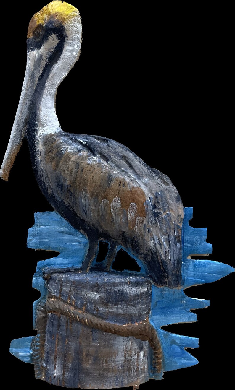 May include: A painted wooden sculpture of a pelican perched on a weathered wooden piling. The pelican has a yellow head, a long gray beak, and brown and gray feathers. The piling is wrapped with a rope and sits in front of a blue water background.