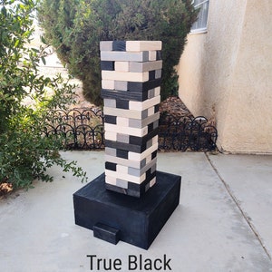 May include: A large wooden block stacking game in shades of black, gray, and natural wood. The game is set on a black base, with the text "True Black" at the bottom. The blocks are arranged in a tower formation.
