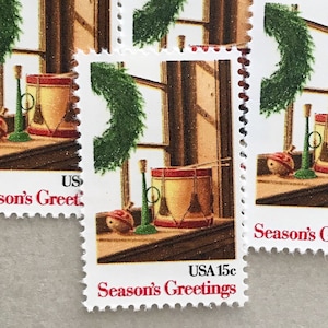 May include: A sheet of vintage US postage stamps featuring a holiday scene. Each stamp depicts a drum, a trumpet, and a Christmas ornament on a windowsill, with a green wreath and the text "Season's Greetings".