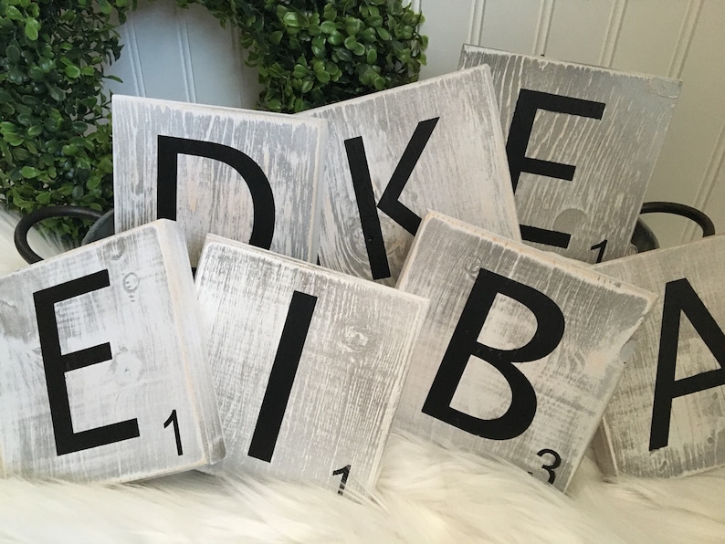 Puede incluir: Azulejos de madera blancos con letras negras que deletrean la palabra "DEIBAK" con los valores de las letras en la parte inferior de cada azulejo.