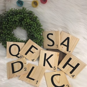 Puede incluir: Azulejos de Scrabble de madera que deletrean el nombre "SAKHL" en letras negras sobre un fondo blanco. Los azulejos est&aacute;n dispuestos en semic&iacute;rculo con la "S" en la parte superior y la "L" en la parte inferior.