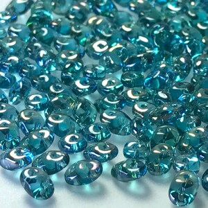 May include: A close-up of a pile of teal blue glass seed beads with an iridescent finish.