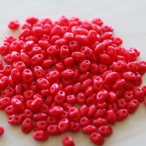 May include: A large pile of small, bright red, oval-shaped glass beads.