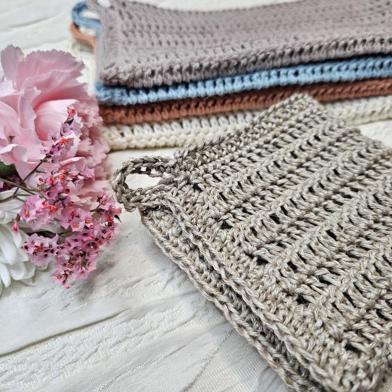 May include: A set of four crocheted dishcloths in various shades of brown, beige, and blue. The dishcloths are made with a textured stitch pattern and have a loop for hanging.