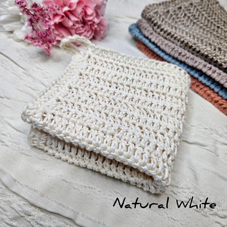 May include: A natural white crocheted washcloth with a textured pattern. The washcloth is folded in half and has a loop for hanging.