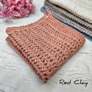 May include: A folded red clay crocheted dishcloth. The dishcloth is made with a simple stitch pattern and has a slightly textured surface.
