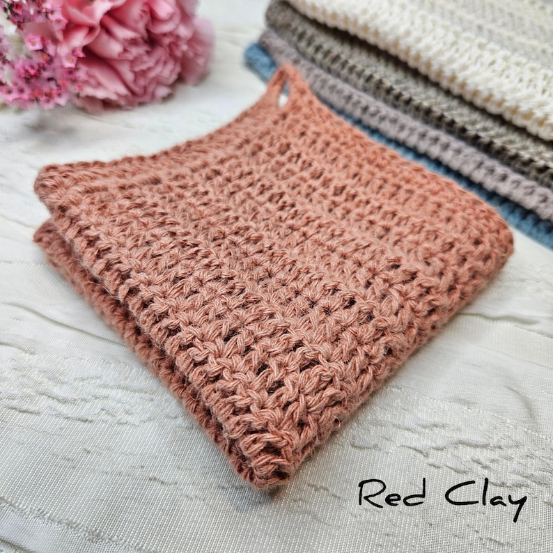 May include: A folded red clay crocheted dishcloth. The dishcloth is made with a simple stitch pattern and has a slightly textured surface.