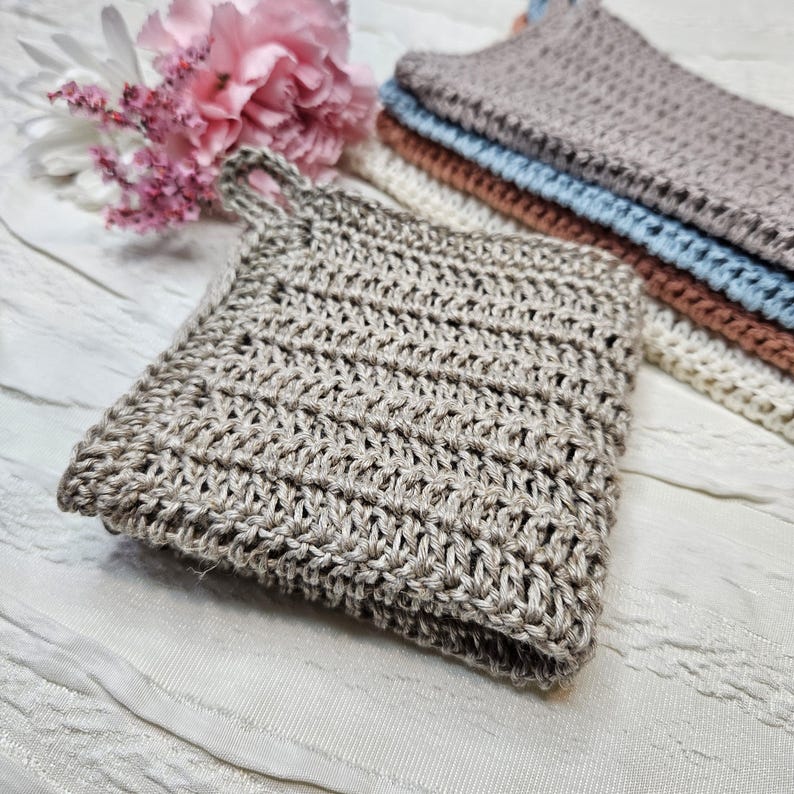 May include: A close-up of a beige crocheted dishcloth with a textured pattern. The dishcloth is folded in half and has a loop handle.
