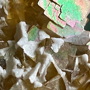 May include: Close-up of a cluster of iridescent, multi-faceted crystals with a white, powdery mineral coating.
