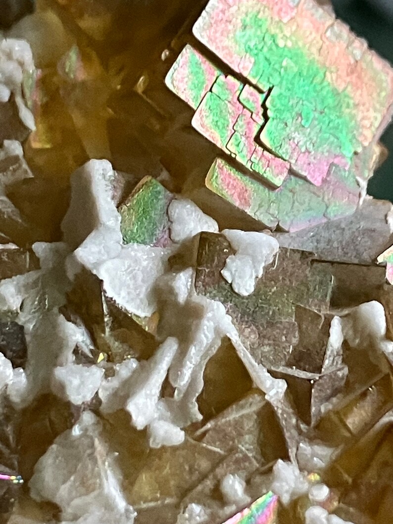 May include: Close-up of a cluster of iridescent, multi-faceted crystals with a white, powdery mineral coating.