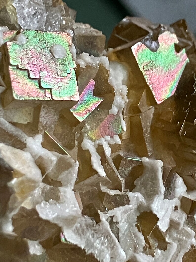 May include: Close-up of a cluster of iridescent brown fluorite crystals with a white mineral matrix. The crystals have a variety of shapes and sizes, and some have a rainbow-like sheen.