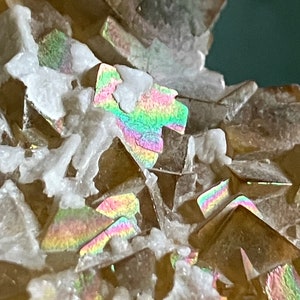 May include: Close-up of a cluster of iridescent brown crystals with a white, powdery matrix. The crystals have a rainbow-like sheen.