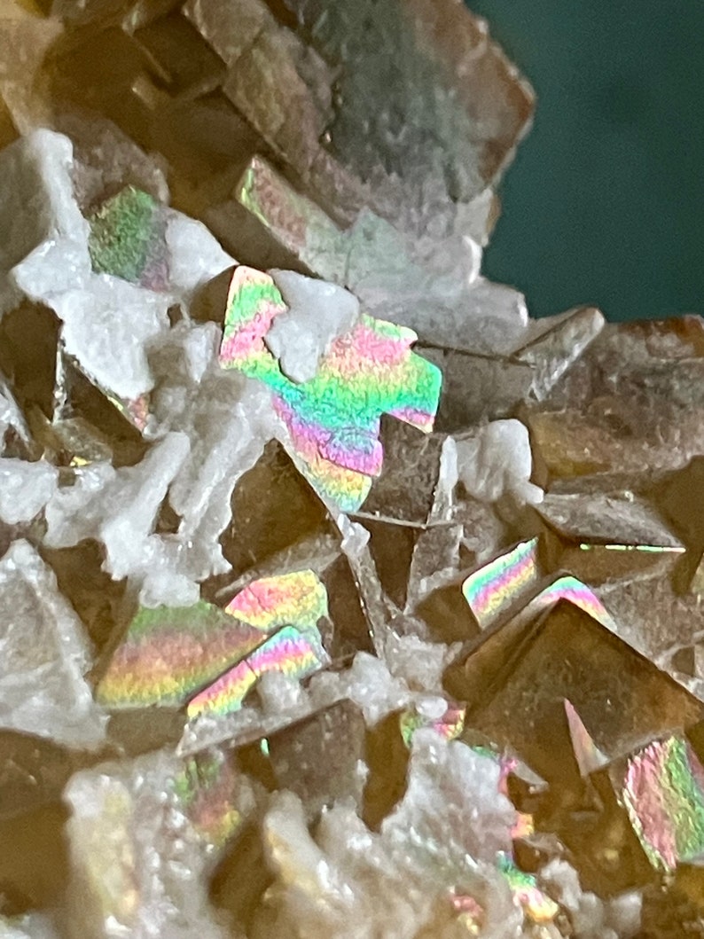 May include: Close-up of a cluster of iridescent brown crystals with a white, powdery matrix. The crystals have a rainbow-like sheen.