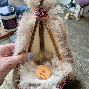 May include: A small wooden teepee with a faux fur exterior. The teepee has a red and blue patterned band around the top and a wooden plaque with the text "Polar Sirkelen Norge" and a reindeer silhouette.