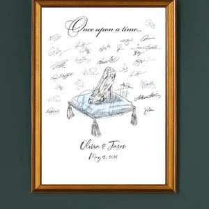 May include: A framed print featuring a Cinderella-style glass slipper on a blue pillow with tassels. The words "Once upon a time..." are at the top, with signatures and the names "Olivia & Jason" and the date "May 15, 2026" below.