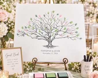 May include: A white canvas guest book print featuring a black ink tree illustration with pink and green fingerprint leaves, personalized with the text STEPHANIE & JACOB and November 12, 2026, displayed on a gold metal easel stand.