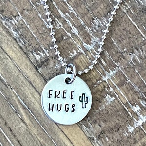 May include: Silver necklace with a round pendant that says "FREE HUGS" with a small cactus graphic.